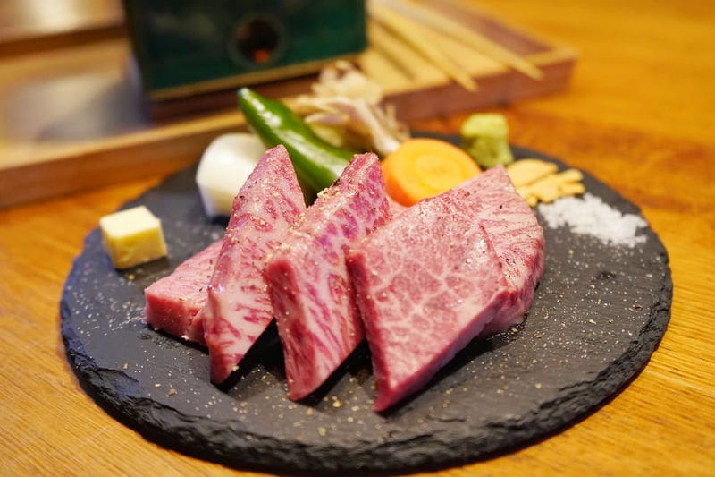 黒くて丸いお皿に熊野牛のお肉が四切れと人参、ピーマン、玉ねぎがのっている。